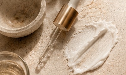 Skincare serum dropper and cream on warm stone